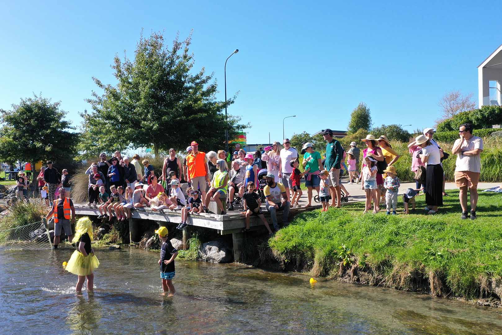 a large group of people gather at the jetty beside the duck race finish line